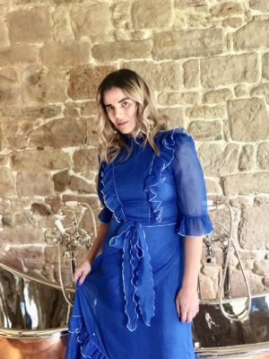 Pixie Tenenbaum wearing a cerulean blue midi vintage prairie dress in the Muckle Hoose Suite at Beadnell Towers Hotel